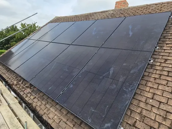 Two rows of black solar panels on a brown tiled roof, with scaffolding and guard rails along the edge