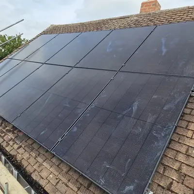 Two rows of black solar panels on a brown tiled roof, with scaffolding and guard rails along the edge