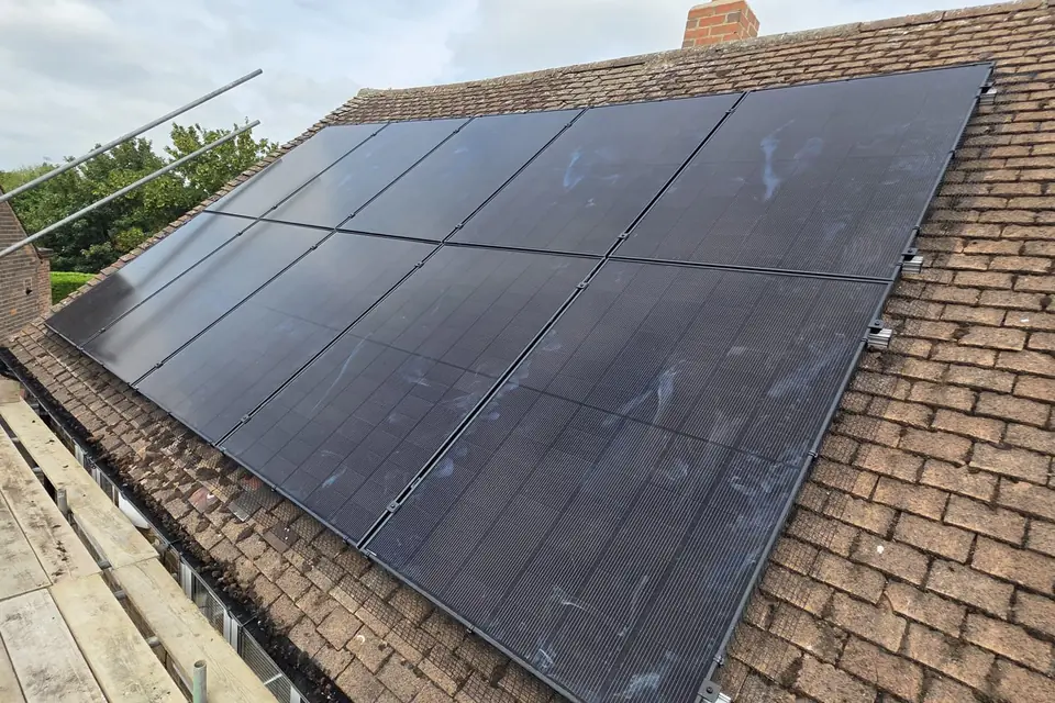Two rows of black solar panels on a brown tiled roof, with scaffolding and guard rails along the edge