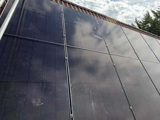 Black solar panels across a red-tiled roof under a blue sky with clouds