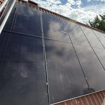 Black solar panels across a red-tiled roof under a blue sky with clouds