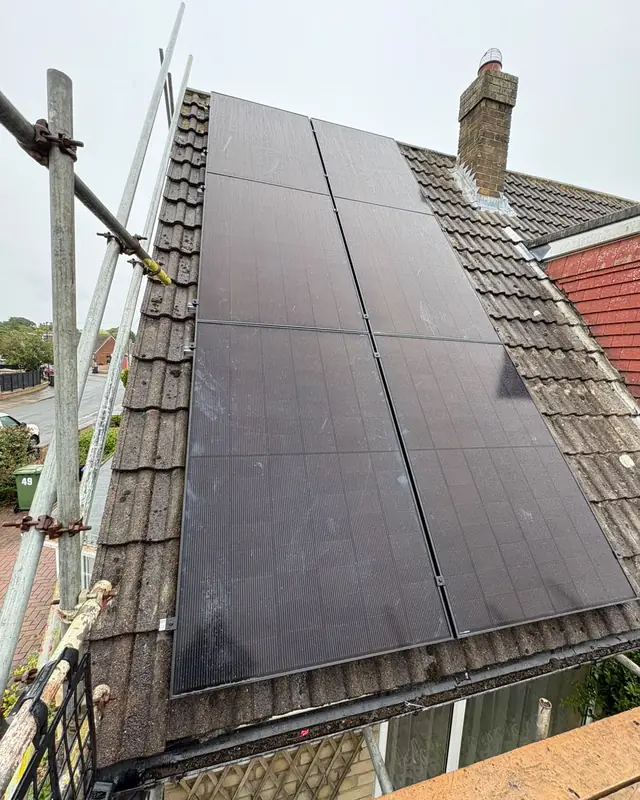 Two columns of black solar panels fitted to the same roof, with scaffolding and guard rails alongside