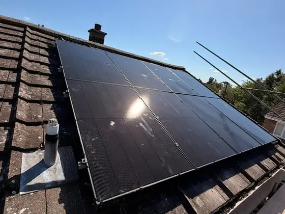 Two rows of black solar panels on a tiled roof beside a chimney, with scaffolding along the edge