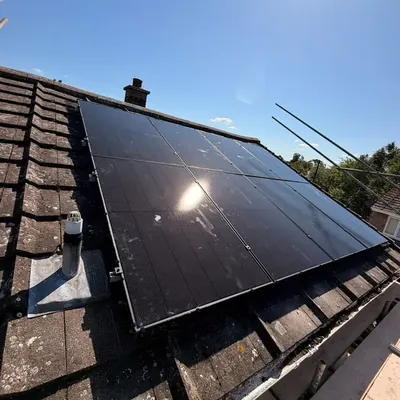 Two rows of black solar panels on a tiled roof beside a chimney, with scaffolding along the edge