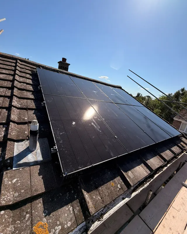 Two rows of black solar panels on a tiled roof beside a chimney, with scaffolding along the edge