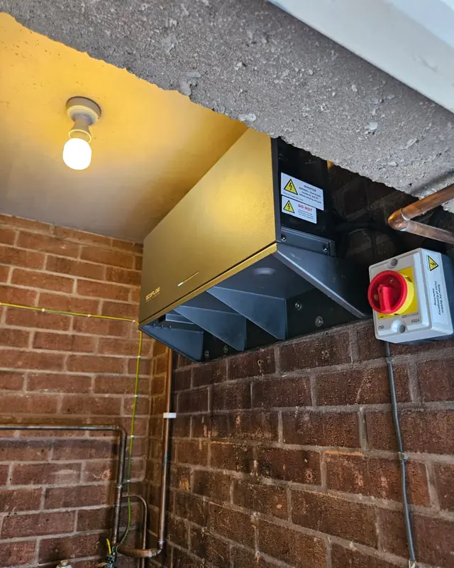 An inverter and a red isolator switch fixed high on a brick wall under a concrete canopy