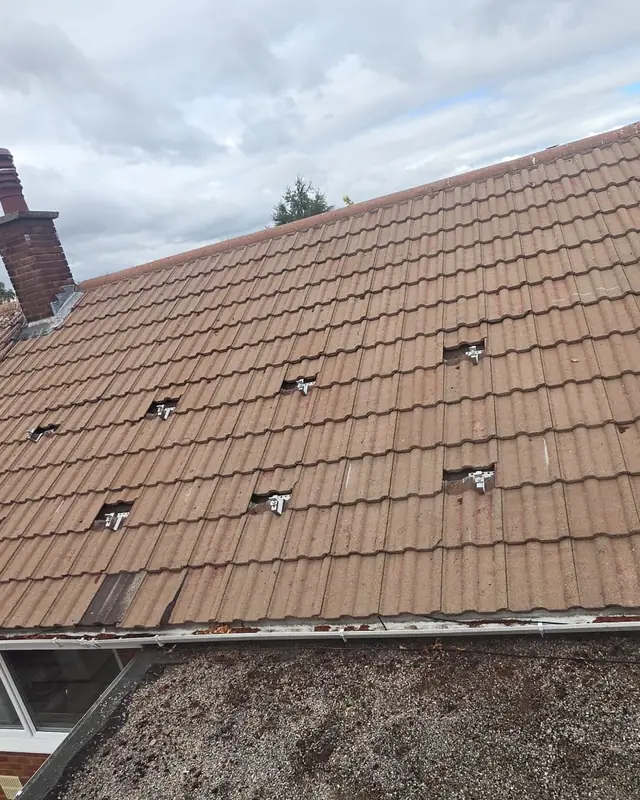 An orange tiled roof with a few tiles lifted where the metal roof hooks for the panels sit