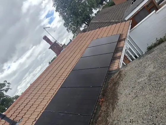 A column of black solar panels on an orange tiled roof, beside a flat roof