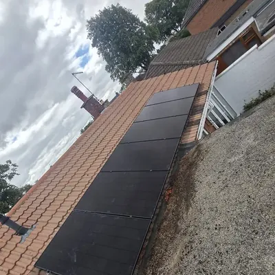 A column of black solar panels on an orange tiled roof, beside a flat roof