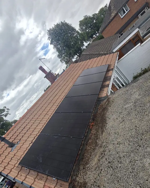 A column of black solar panels on an orange tiled roof, beside a flat roof