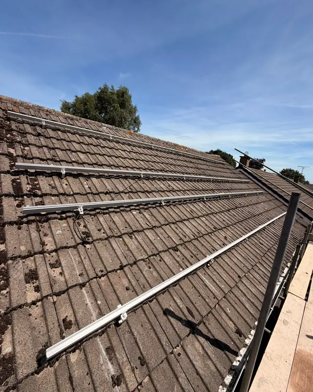 Aluminium mounting rails fixed across a concrete-tiled roof under a blue sky, ready for the solar panels