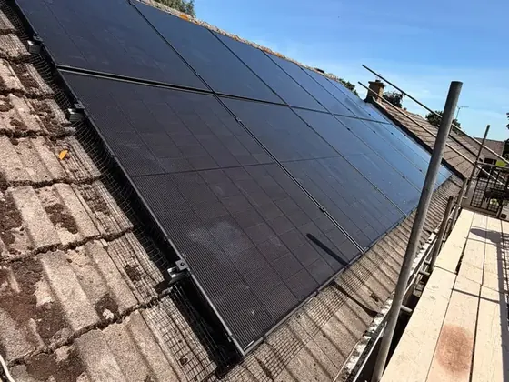 Black solar panels on a concrete-tiled roof with bird mesh around the edge, seen from the scaffolding