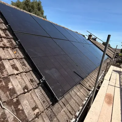 Black solar panels on a concrete-tiled roof with bird mesh around the edge, seen from the scaffolding