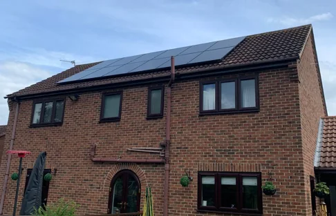 Two rows of black solar panels across the roof of a red-brick two-storey house