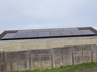Two rows of black solar panels on the roof of a single-storey home, seen over a garden fence