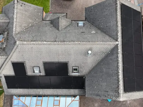 A detached house seen from above, with black solar panels on two roof faces, fitted around two roof windows