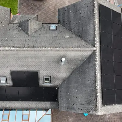 A detached house seen from above, with black solar panels on two roof faces, fitted around two roof windows