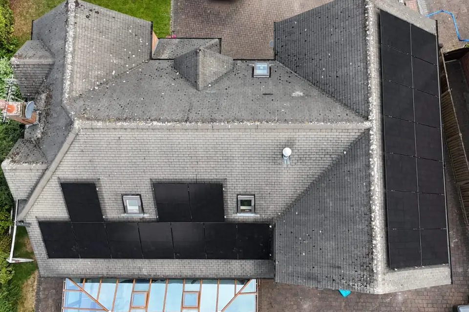 A detached house seen from above, with black solar panels on two roof faces, fitted around two roof windows